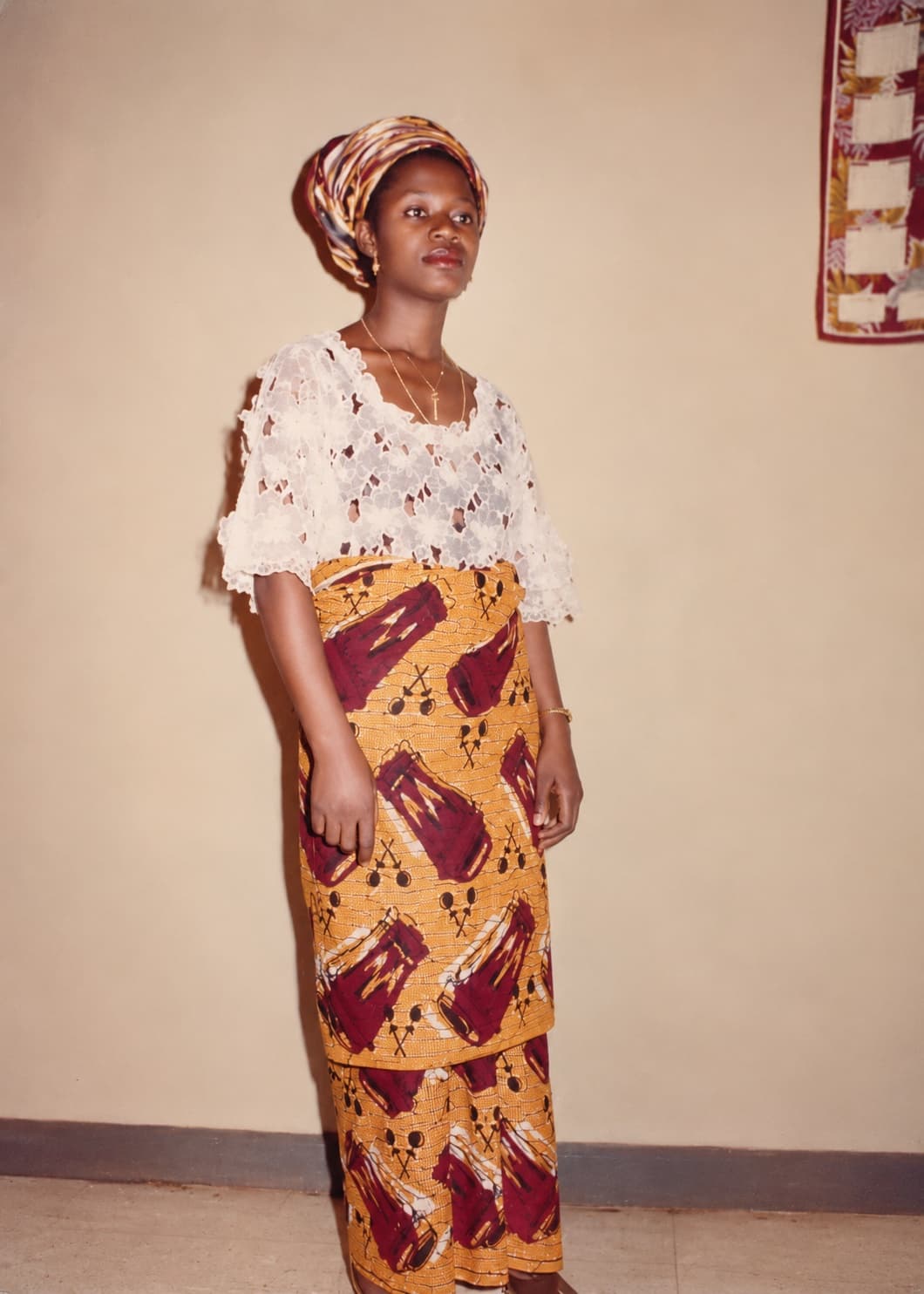 Mrs Egbo as a young woman in a white lace blouse, a gold and maroon print wrapper, and a matching headwrap